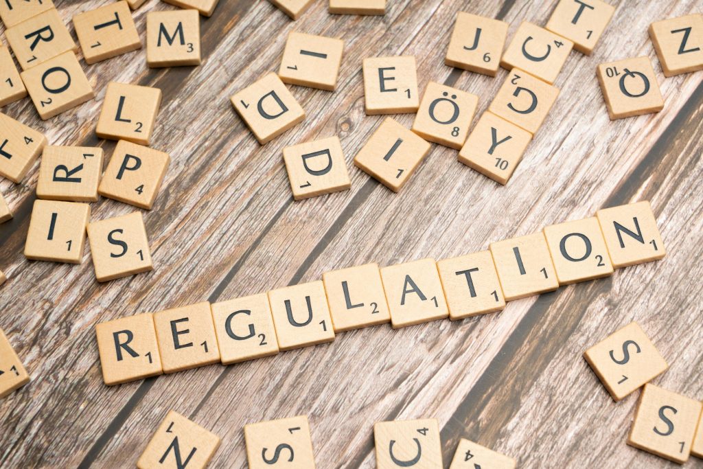 Regulatory Advisory Wooden letter tiles spelling 'Regulation' on a textured wood background, conveying themes of compliance and structure.