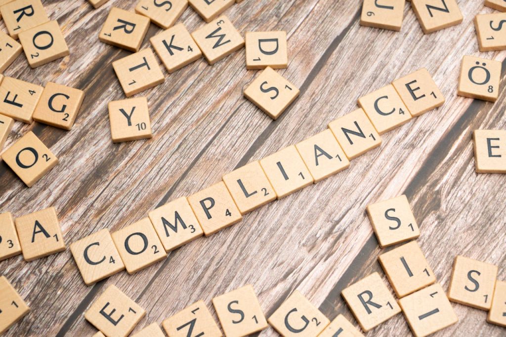 Compliance Framework Wooden letter tiles forming the word 'COMPLIANCE' on a rustic wooden background.
